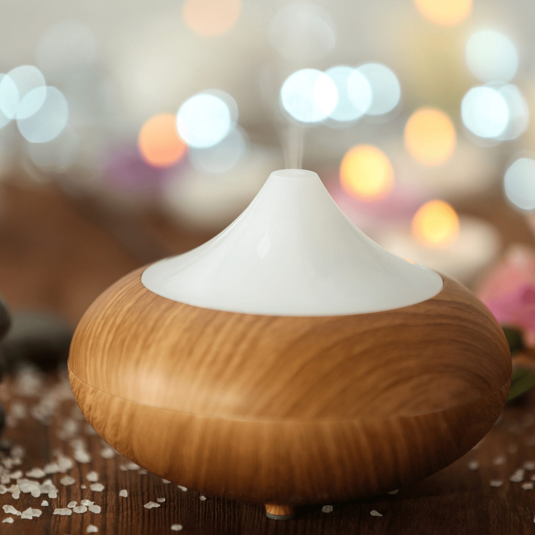 white and wood essential oil diffuser sitting on a table with colorful lights blurred in the background