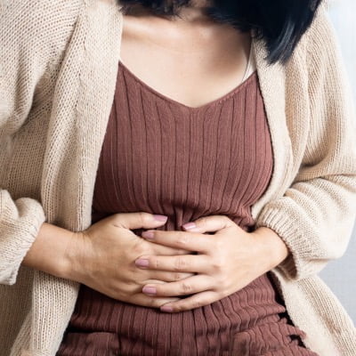 Natural Remedies for an Upset Stomach - woman standing and holding her stomach in pain